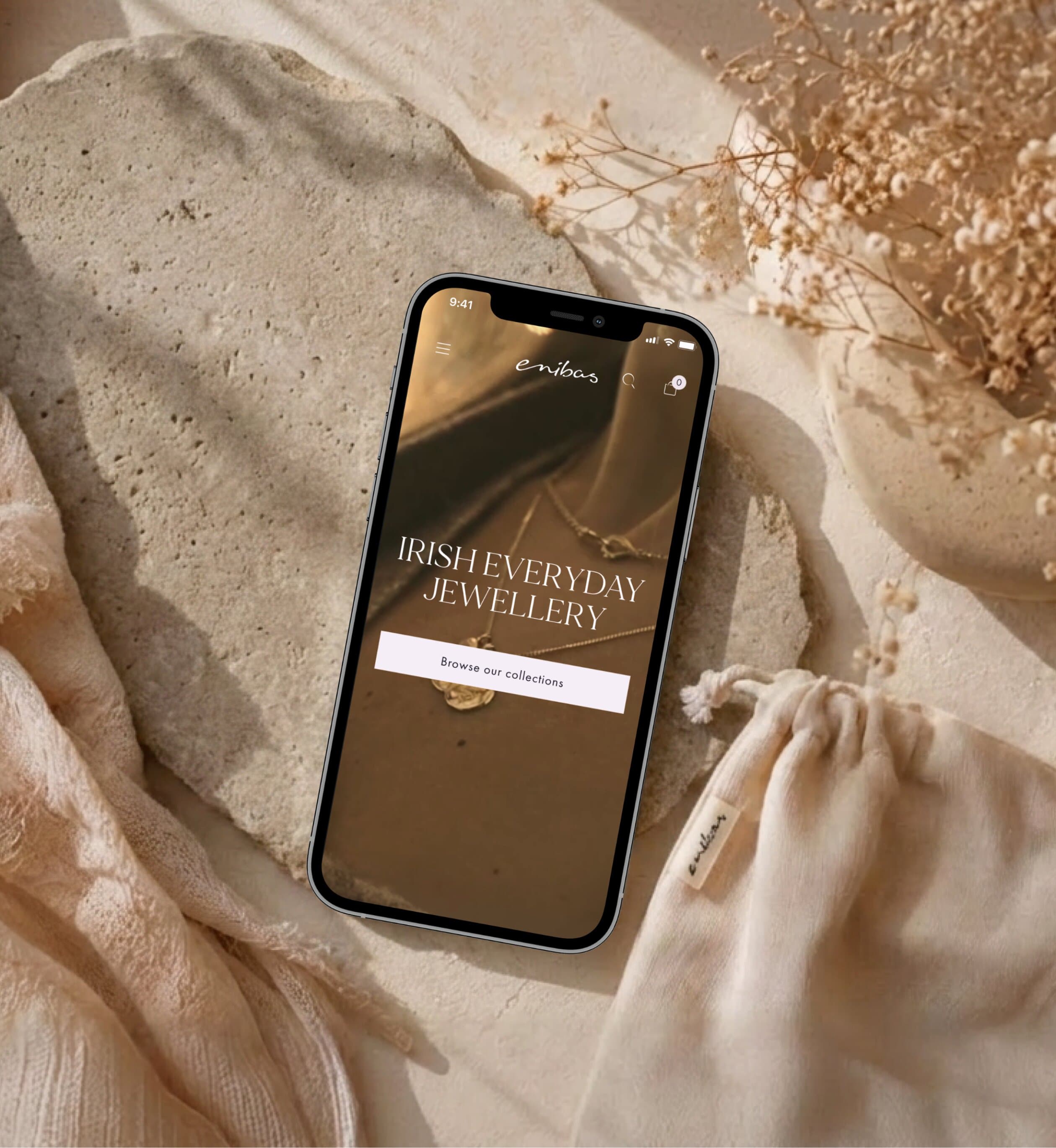 Enibas Schmuck-Store auf einem Smartphone, umgeben von Sand und natürlichen Requisiten