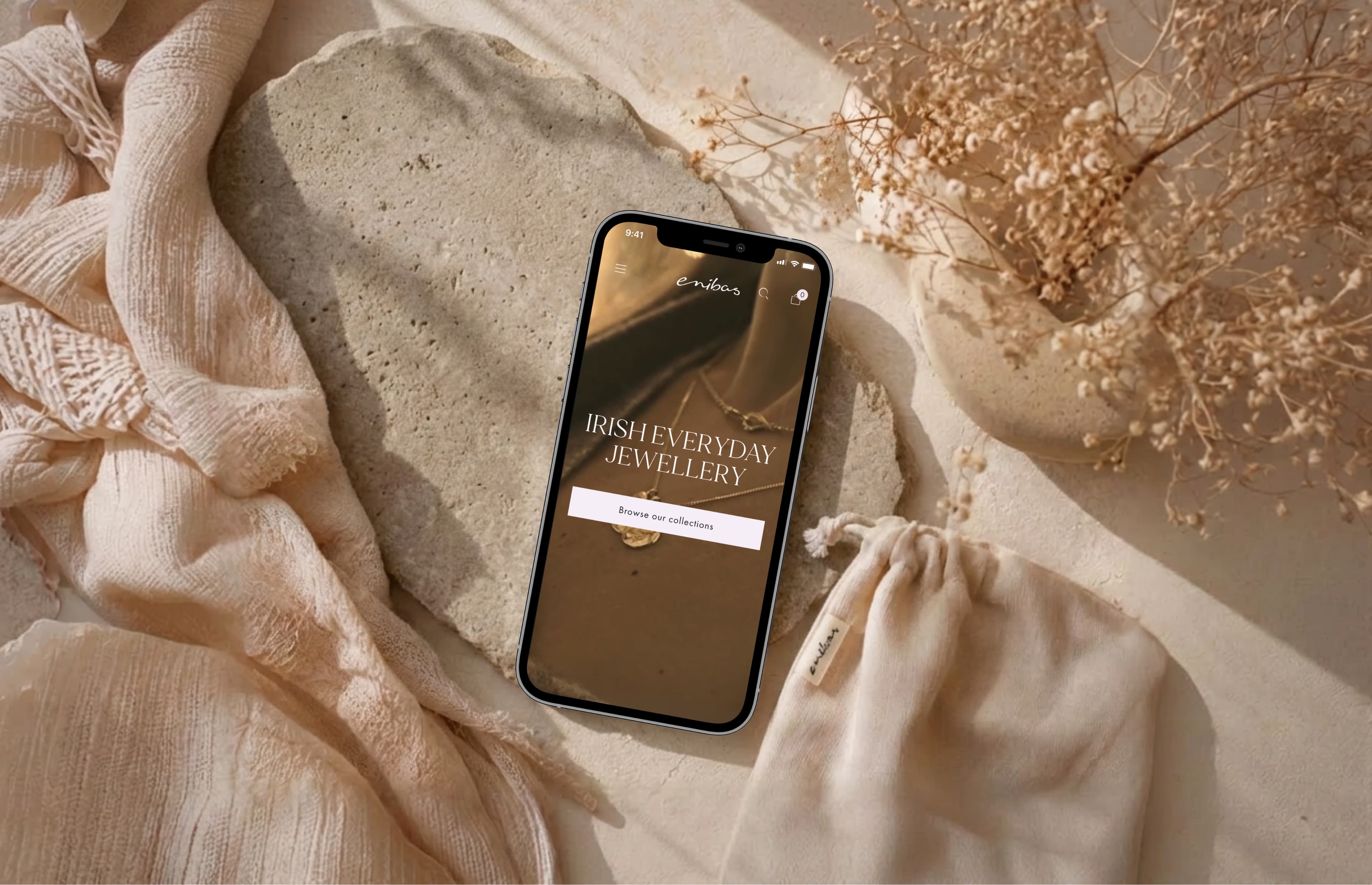 Der Enibas Schmuck-Store auf einem Smartphone, umgeben von weichen Stoffen und Trockenblumen